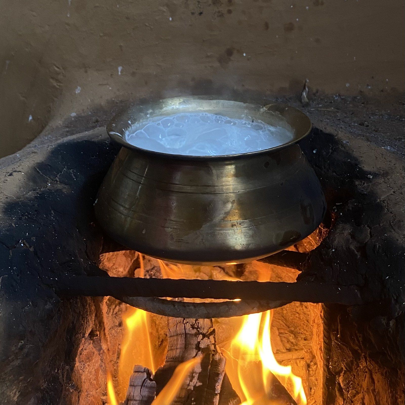 A metal pot simmering over a wood fire in a rustic kitchen