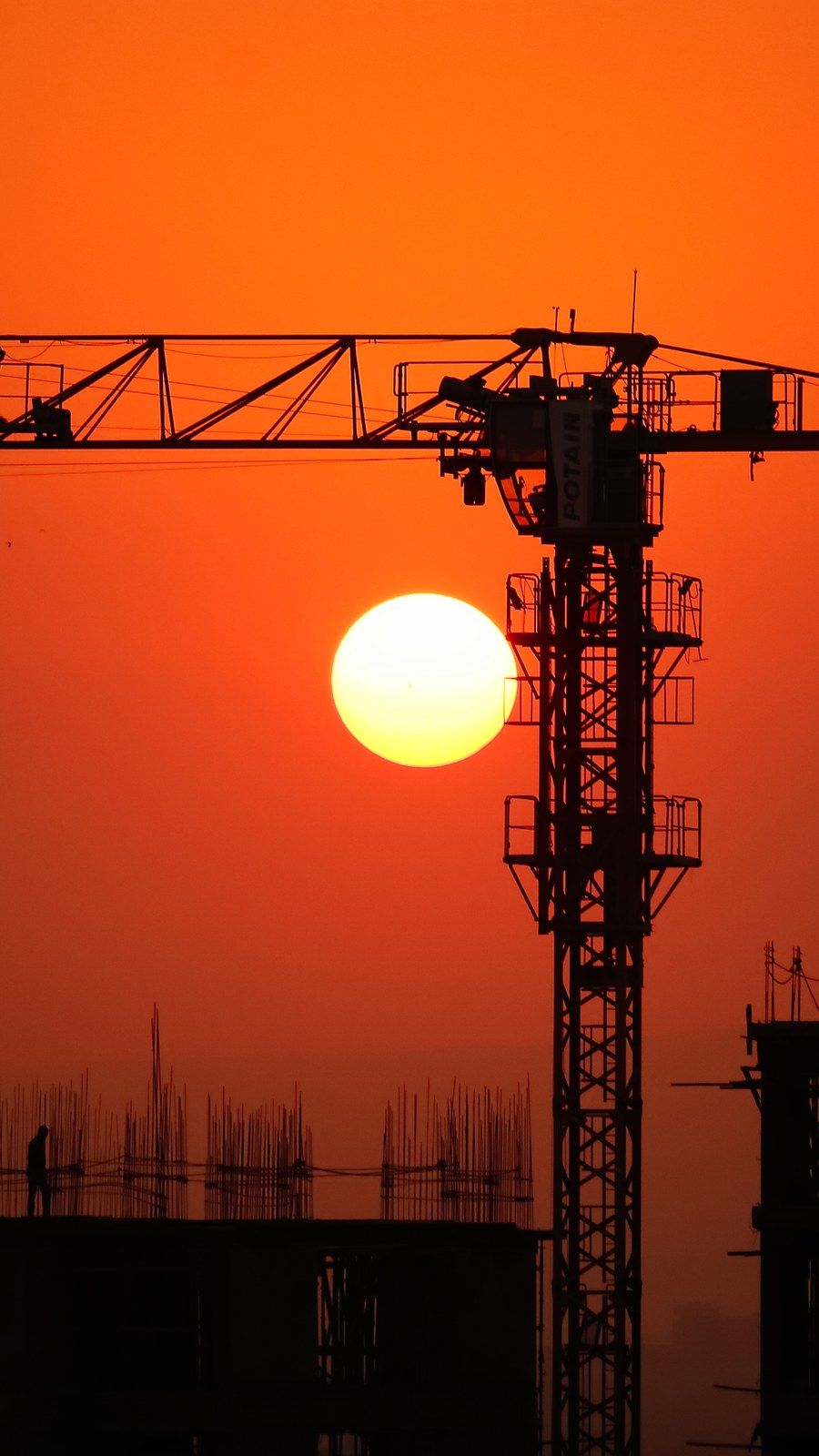 Silhouette of a construction crane above an unfinished building against an orange sunset