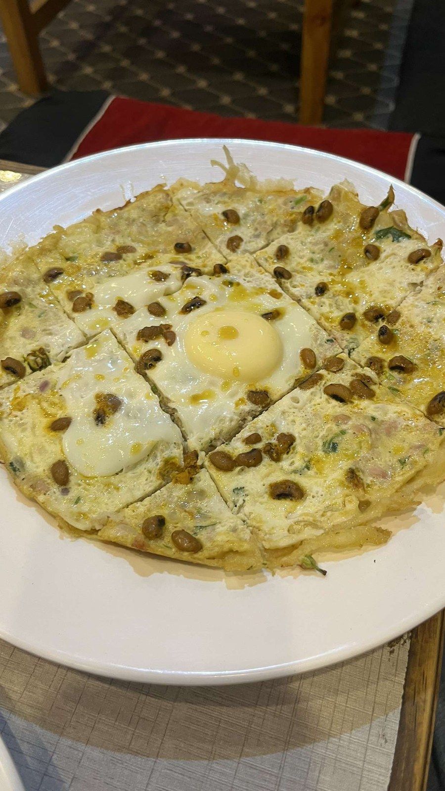 A savoury rice crêpe topped with an egg and seeds on a white plate, seen from above