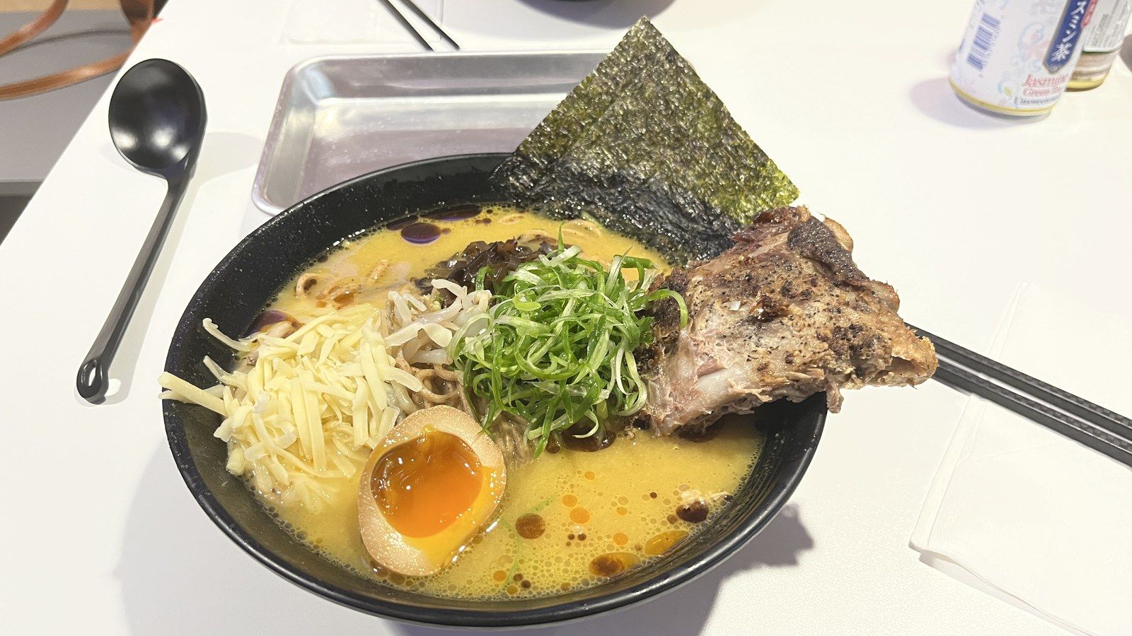 Bowl of pork rib ramen with noodles, a soft-boiled egg, spring onions and a sheet of nori