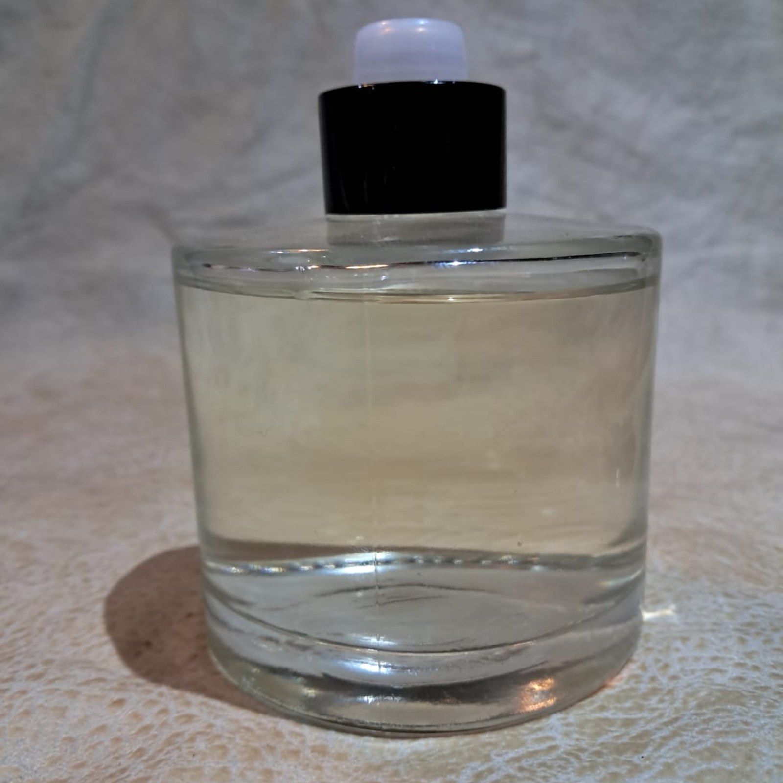 A clear glass bottle with a black cap standing on a crumpled cream fabric